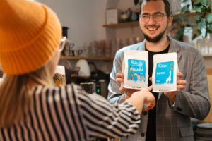 by jak najdłużej cieszyć się świeżością kawy, warto stosować się do kilku prostych zasad: a) Przechowywanie w szczelnym opakowaniu Najlepszym rozwiązaniem są opakowania z zaworem jednokierunkowym, które pozwalają na uwalnianie CO₂, ale nie wpuszczają tlenu do środka. Jeśli kawa jest pakowana w folię, warto przesypać ją do szczelnego pojemnika po otwarciu. b) Unikanie światła i wilgoci Kawę należy przechowywać w ciemnym i suchym miejscu, np. w szafce kuchennej z dala od okna. Nie należy trzymać kawy w lodówce, ponieważ wilgoć i zmiany temperatury mogą negatywnie wpłynąć na jej jakość. c) Przechowywanie w formie ziaren Kawę najlepiej kupować w ziarnach i mielić tuż przed zaparzeniem. Zmielona kawa traci świeżość znacznie szybciej ze względu na większą powierzchnię kontaktu z powietrzem.