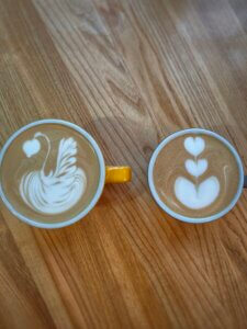 Dwie filiżanki kawy latte i cappuccino z latte art w kształcie serca i łabędzia na drewnianym stole w kawiarni