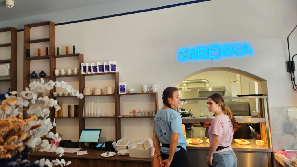 Regał z paczkami kawy Syrenka i filiżankami obok wydawki w restauracji Syrenka