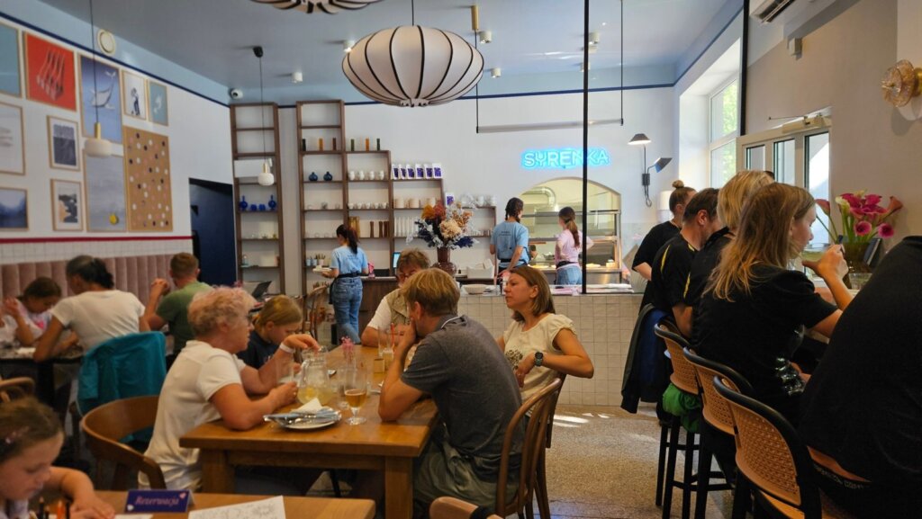 Wnętrze restauracji Syrenka w Kołobrzegu, goście przy stołach i bar z neonem