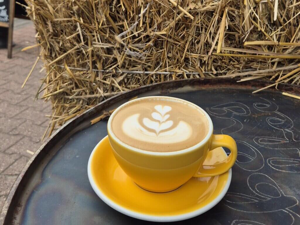 Latte w żółtej filiżance na stoliku w jesiennym ogródku kawiarni Colbergcoffee