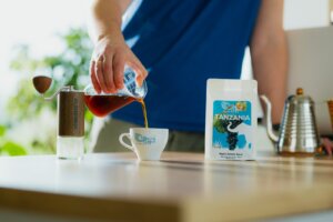 Kawa przelewowa nalewana z serwera do filiżanki, obok młynek ręczny i kawa Colbergcoffee